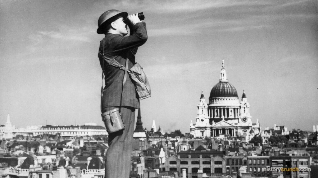A British spotter scans the sky over London with binoculars from a rooftop during World War II, with St. Paul's Cathedral visible in the background.