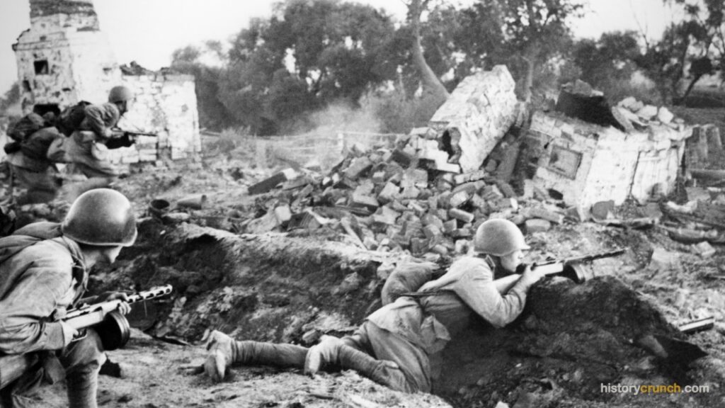 Soviet soldiers fire from a trench and ruined buildings during ground combat on the Eastern Front in World War II.