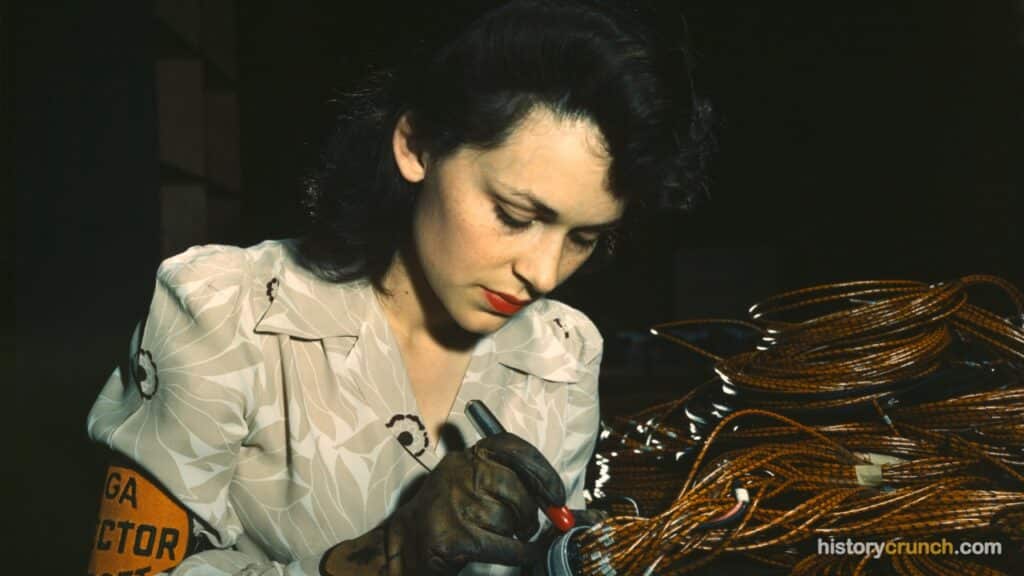 A woman wearing an inspector's armband checks wiring components at a U.S. defense plant during World War II, when millions of American women took on factory jobs to support the war effort.